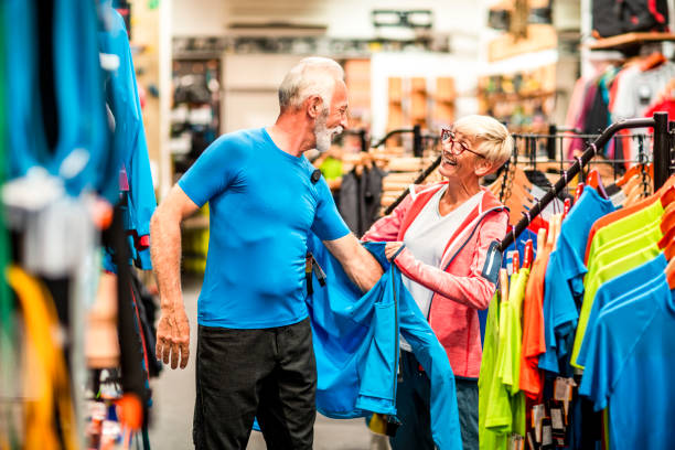 istock Senior active man putting on a soft shell hiking jacket while his partner is helping him in a mountaineering equipment store 1230907411