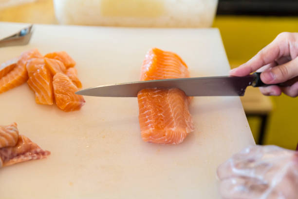 istock Chef use knife preparing a fresh salmon on a cutting board, Japanese chef in restaurant slicing raw salmon, ingredient for seafood dish. Chef with a knife cutting raw salmon. 1230934531
