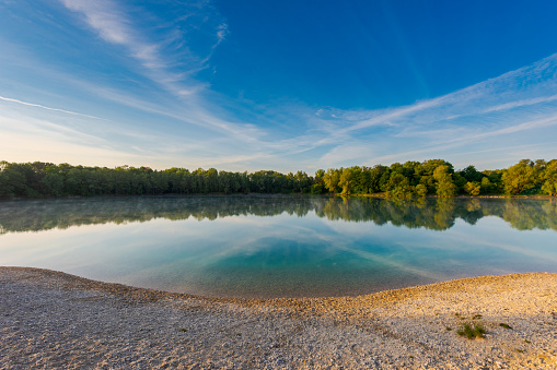 Small local recreation swimming lake in Bavaria, Germany in early morning light with fog over water