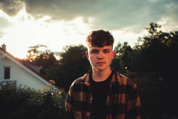 Young teenage man dressed with plaid shirt standing outdoors in his residential suburban district in sunset light. South German Suburb Millennial Youth Culture Outdoor Portrait.