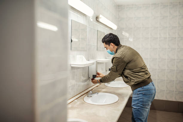 istock Man with a face mask washes his hands in a public bathroom 1230980946