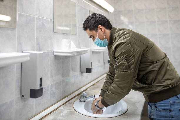 istock Man with a face mask washes his hands in a public bathroom 1230982468