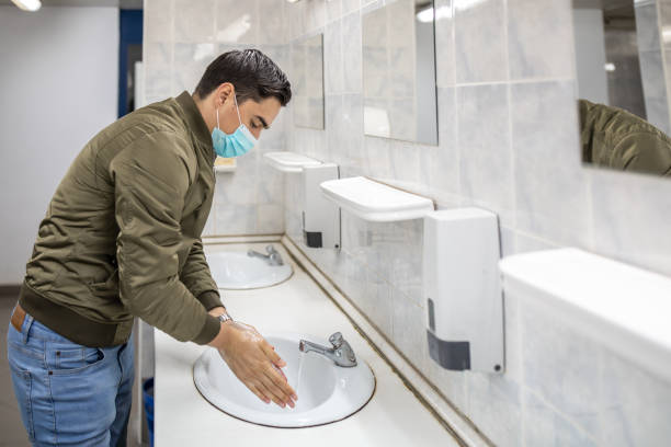 istock Man with a face mask washes his hands in a public bathroom 1230982614