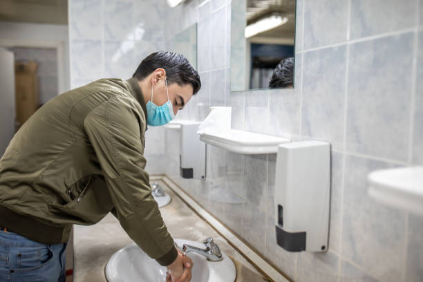 istock Man with a face mask washes his hands in a public bathroom 1230985510