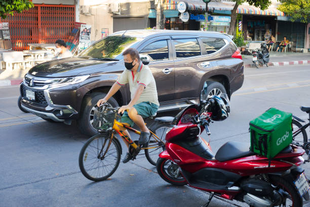 mature thai man with mask on bicyle is overtaken by car - overtaken imagens e fotografias de stock