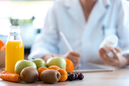 Mujer nutricionista médico escribe la prescripción médica para una dieta correcta en un escritorio con frutas, píldoras y suplementos. photo