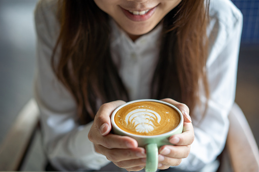 Young asian woman holding a cup of frothy flat white coffee with coffee froth art