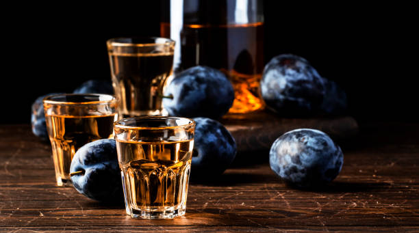 slivovica - brandy de ciruela o vodka ciruela, licor duro balcánico, bebida fuerte en vasos de tiro en la vieja mesa de madera, copiar el espacio - slivovitz fotografías e imágenes de stock