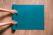 Woman folding blue exercise mat on wooden floor.