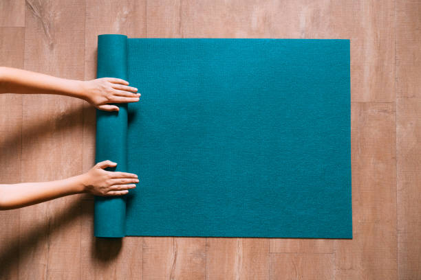 Woman folding blue exercise mat on wooden floor. Fit woman folding blue exercise mat on wooden floor before or after working out in yoga studio or at home. Equipment for fitness, pilates or yoga, well being concept. Flat lay, space for text. mat photos stock pictures, royalty-free photos & images