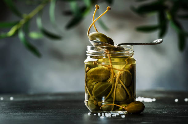 Capers. Marinated or pickled canned capers fruit close up in glass jar on gray kitchen table background. Copy space