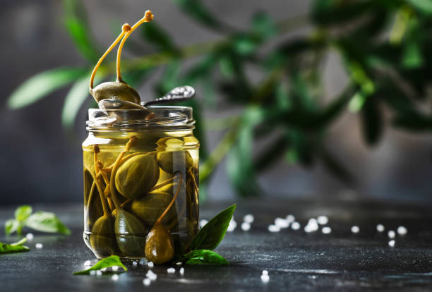 istock Capers. Marinated or pickled canned capers fruit close up in glass jar on gray kitchen table background. Copy space 1231209267