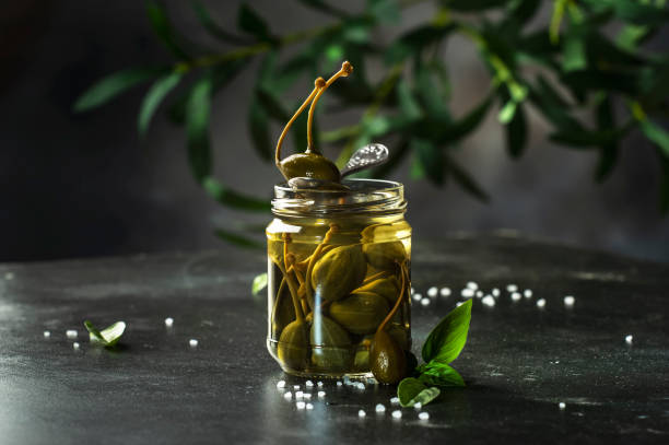 istock Capers. Marinated or pickled canned capers fruit close up in glass jar on gray kitchen table background. Copy space 1231210234