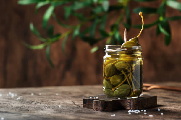 istock Capers. Marinated or pickled canned capers fruit in glass jar on wooden table background. Space for text 1231211772