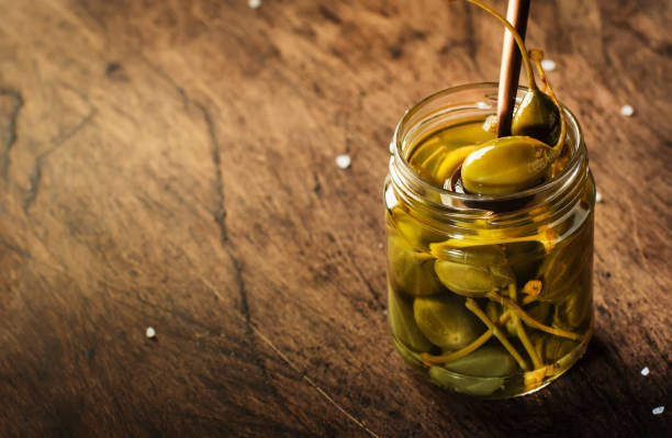 istock Capers. Marinated or pickled canned capers fruit in glass jar on wooden table background. Space for text 1231212280