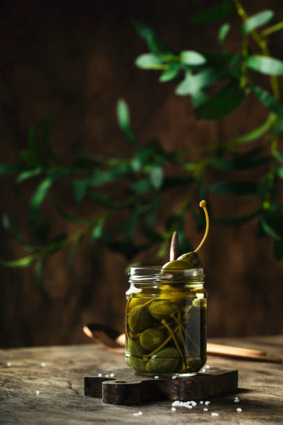 istock Capers. Marinated or pickled canned capers fruit in glass jar on wooden table background. Space for text 1231212788