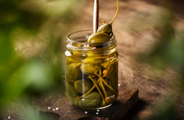 istock Capers. Marinated or pickled canned capers fruit in glass jar on wooden table background. Space for text 1231213294