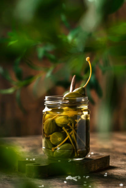 istock Capers. Marinated or pickled canned capers fruit in glass jar on wooden table background. Space for text 1231213803