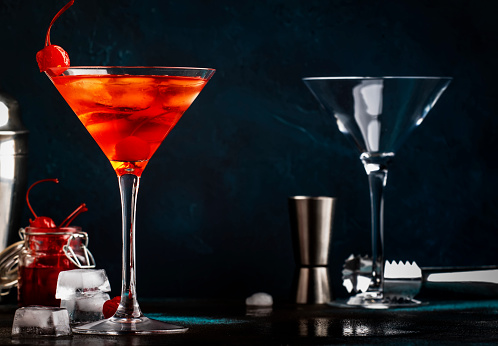 Manhattan alcoholic cocktail with bourbon, red vermouth, bitter, ice and cocktail cherry in glass, night mood image, copy space