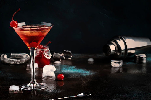 Manhattan alcoholic cocktail with bourbon, red vermouth, bitter, ice and cocktail cherry in glass, night mood image, copy space