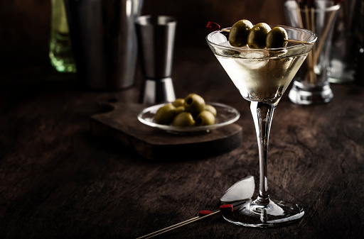 glass with brown alcoholic drink and piece of ice stands on the bar. Blurred view of restaurant in background.