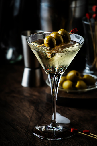 Martini cocktail, with dry vermouth, vodka and green olives, vintage wood bar counter with bar tools