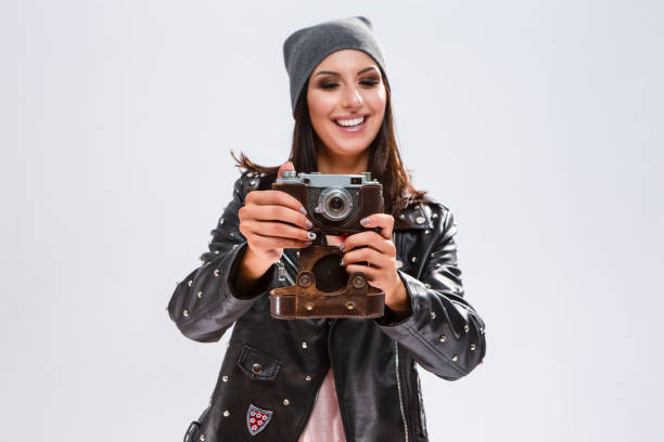 istock Modern Lifestyle Ideas. Open Happy Caucasian Brunette in Black Leather Jacket Posing With Old School Film Photocamera. Against White.Focus on Camera. Horizontal Image Composition 1231277359