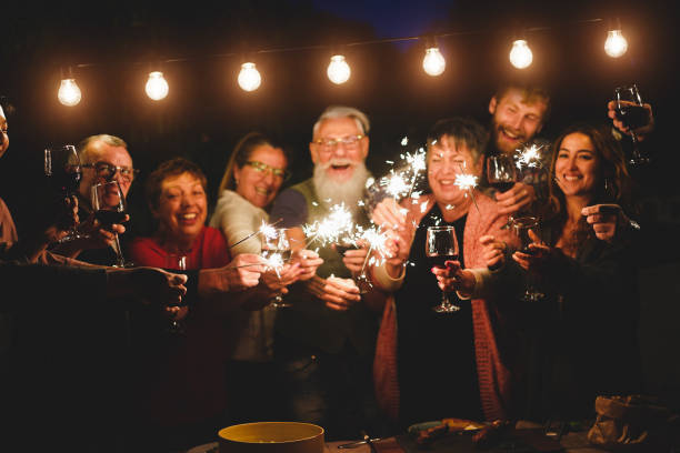 Happy family and friends celebrating with sparkler fireworks at home dinner - Different age of people having fun together in patio party - Celebration and summer holidays concept - Focus on left hands feliz familia y amigos celebrando con fuegos artificiales de chispas en la cena en casa - diferente edad de personas divirtiéndose juntos en la fiesta del patio - celebración y días festivos de verano concepto - enfoque en las manos izquierdas