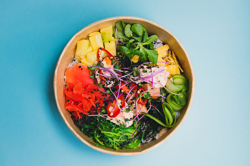 View tasty poke bowl with salmon, mango, ginger and rice on the blight blue flat lay - traditional Asian and Hawaiian street food