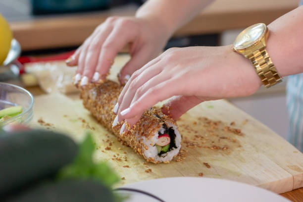 istock Female hands rolling a sushi in fried sesame seeds. Making a complicated dish like sushi at home 1231408595