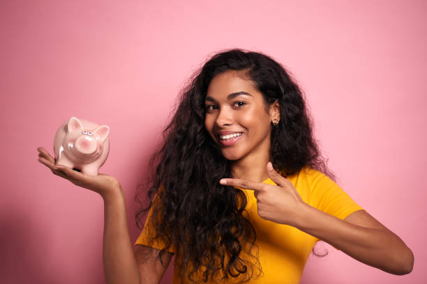 Smiling African woman pointing the piggy bank in studio shot. Smiling African woman pointing the piggy bank in studio shot. animal representation photos stock pictures, royalty-free photos & images