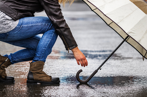 Selective focus at female hand and handle of umbrella. Rainy day and wind in city