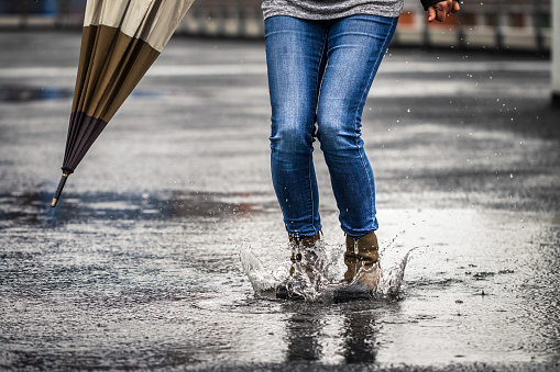 Woman holding umbrella and standing on street during bad weather. Female legs wearing jeans and leather boot. Rainy season in city