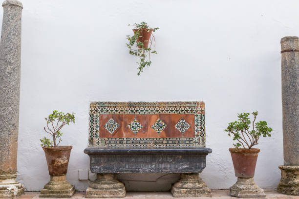masonry bench with decorative tiles, on the sides two pots with plants with a white background, patio of Cordoba, harmonious composition