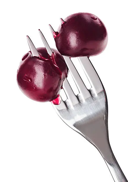 Two bloody cherry fruits pricked on metal fork, isolated on white