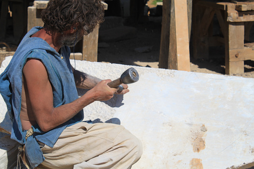 Guedelon castle, Treigny, France - May 28, 2012: Sculptor working a block of stone with a chisel in Guedelon castle. In the heart of Puisaye, in Yonne, Burgundy, a team of fifty people have taken on an extraordinary feat: to build a castle using the same techniques and materials used in the Middle Ages.