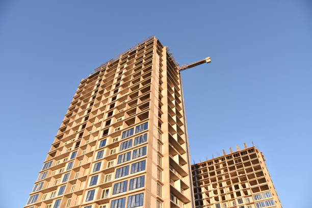 istock Construction the high-rise building. Installation of double-glazed windows with uPVC frames in new residential skyscraper on blue sky background. Tall house renovation project, government programs 1231630520