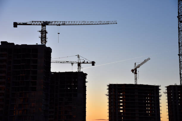 istock Silhouettes of tower cranes constructing a new residential building at a construction site on sunset background. Crane lifting a concrete bucket. Builders pouring cement mix for formworks. Soft focus 1231655604