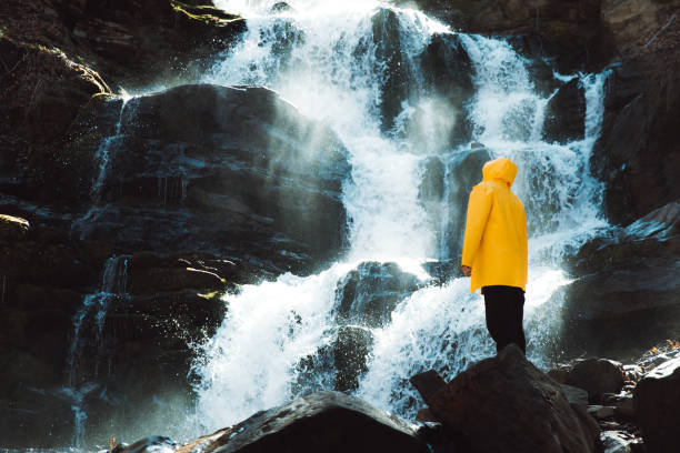 istock Young man in yellow raincoat exploring the beautiful sunny waterfall in the mountains 1231686320