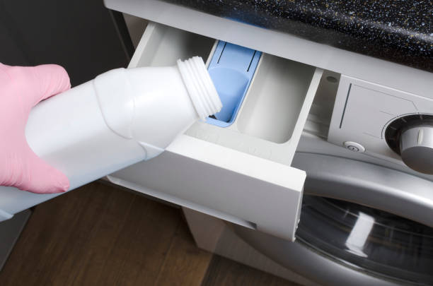 woman wearing protective pink gloves and pouring liquid detergent into the washing machine.household routines - liquid soap blue plastic textile imagens e fotografias de stock