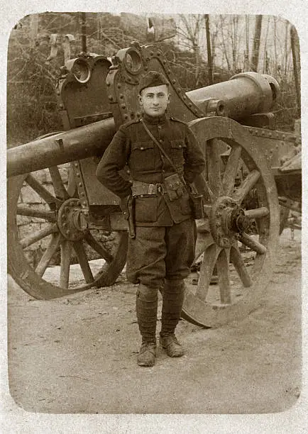 Soldier from WWI stands in uniform in front of cannon.