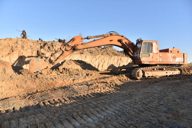 Excavator working at open pit mining. Backhoe digs ground in sand quarry on blue sky background. Construction machinery for excavation, loading, lifting and hauling of cargo on job sites