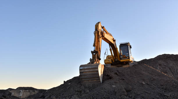 istock Yellow excavator during earthmoving at open pit on blue sky background. Construction machinery and earth-moving heavy equipment for excavation, loading, lifting and hauling of cargo on job sites 1231760397