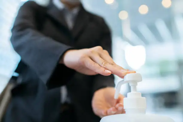 A close up photo of a businesswoman while applying alcohol hand sanitizer at the entrance hall of an office building.