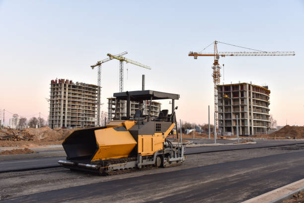 istock Asphalt paver machine during road works. Road Machinery at construction site. Paving roller machine on paving works. Tower cranes constructing a new residential building on sunset 1231792099