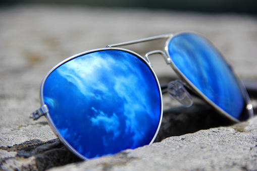 Blue sunglasses on stone withe reflection from sun and clouds