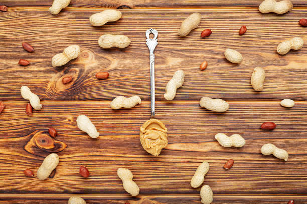 Vintage spoon with creamy peanut butter on a brown wooden table. Near the peanut butter lies peanuts in the shell and peeled peanuts.Flat lay of peanut paste for cooking breakfast. Vegan food concept cuchara vintage con mantequilla de maní cremosa sobre una mesa de madera marrón. cerca de la mantequilla de maní se encuentra cacahuetes en la cáscara y cacahuetes pelados. planta plana de pasta de cacahuete para cocinar el desayuno. concepto de comida