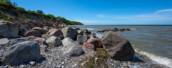 Big stones on the beach in front of the steep coast at the Baltic Sea, blue sky with copy space, panoramic format