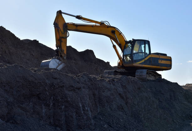 istock Excavator working at open pit mining. Backhoe digs gravel in sand quarry on blue sky background. Recycling old asphalt at a landfill for the disposal of construction waste 1231806196