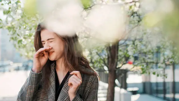 Photo of Springtime allergy. Woman sneezing on the city street